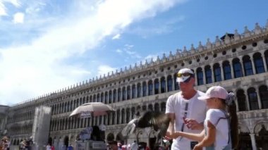 Venice, İtalya - 7 Temmuz 2018: mutlu bir adam ve çocuk kız, turistler, besleme, güvercin, oyun ile onları, holding görünümünü Piazza San Marco, St Marks Bazilikası, bir yaz gününde eğleniyor