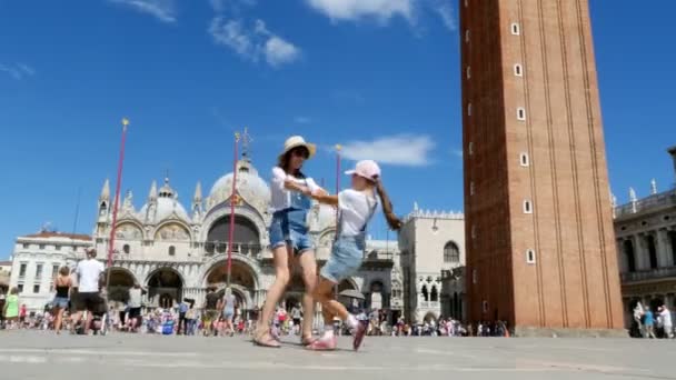 ВЕНИЦА, ИТАЛИЯ - 7 июля 2018 года: вид счастливой красивой женщины и девочки, туристы, держащиеся за руки, кружащиеся на площади Сан-Марко, базилика Святого Марка, в летний день — стоковое видео