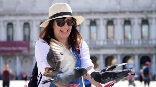 ВЕНИЦА, ИТАЛИЯ - 7 ИЮЛЯ 2018 года: портрет счастливой женщины, туриста, держащего голубей, кормящего, играющего с ними, развлекающегося на площади Сан-Марко, базилика Святого Марка, в летний день — стоковое видео