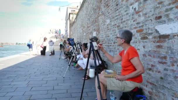 VENECIA, ITALIA - 7 DE JULIO DE 2018: en el muelle de Venecia, muchos artistas, un grupo de adultos, estudiantes de la escuela de arte tienen una lección de dibujo, pintar el paisaje marino. verano día caliente . — Vídeos de Stock