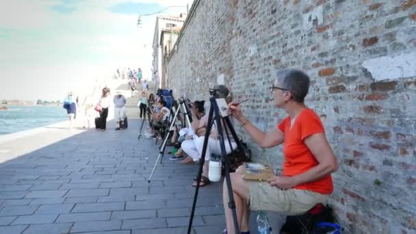 VENECIA, ITALIA - 7 DE JULIO DE 2018: en el muelle de Venecia, muchos artistas, un grupo de adultos, estudiantes de la escuela de arte tienen una lección de dibujo, pintar el paisaje marino. verano día caliente . — Vídeo de stock