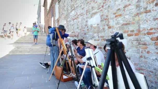 Βενετία, Ιταλία - 7 Ιουλίου 2018: στην προβλήτα της Βενετίας, πολλοί καλλιτέχνες, μια ομάδα ενηλίκων, σπουδαστές της Σχολής τέχνης κρατήστε ένα μάθημα του σχεδίου, χρωματίστε το θαλασσινό τοπίο. ζεστή μέρα του καλοκαιριού. — Αρχείο Βίντεο