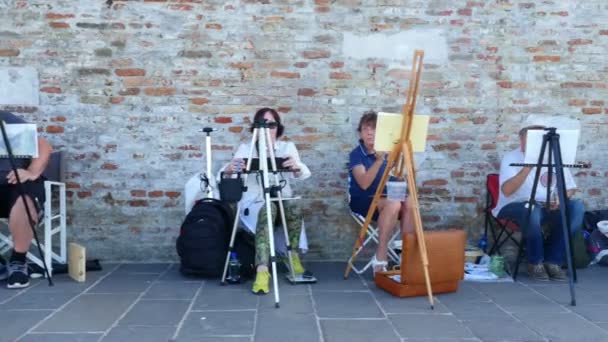 VENECIA, ITALIA - 7 DE JULIO DE 2018: en el muelle de Venecia, muchos artistas, un grupo de adultos, estudiantes de la escuela de arte tienen una lección de dibujo, pintar el paisaje marino. verano día caliente . — Vídeo de stock