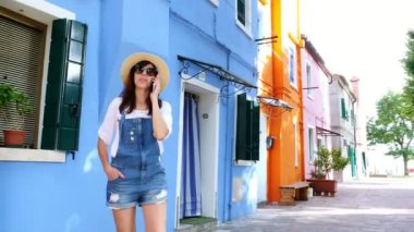 Venedik, Burano, İtalya - 7 Temmuz 2018: genç kadın, kız, Evet güneş gözlüğü, şapka, şort, gülümseyen. Venedik yakınındaki çok renkli evlerin Burano adası.