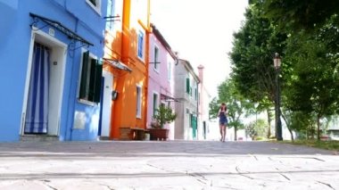 Venedik, Burano, İtalya - 7 Temmuz 2018: genç kadın, kız, Evet güneş gözlüğü, şapka, şort, gülümseyen. Venedik yakınındaki çok renkli evlerin Burano adası.