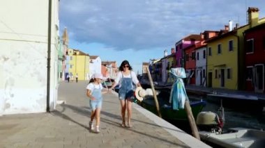 Venedik, Burano, İtalya - 7 Temmuz 2018: genç bir kadın ve bir çocuk kız aynı denim tulum, şort, Burano küçük kanal çalıştırın. sıcak yaz günü.