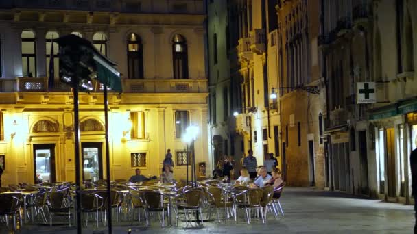 Venedig, Italien - 7 juli 2018: natt utsikt över Venedig. I torget sitter turister vid borden av ett mysigt café, av lyktor ljus. antik arkitektur i Venedig. — Stockvideo