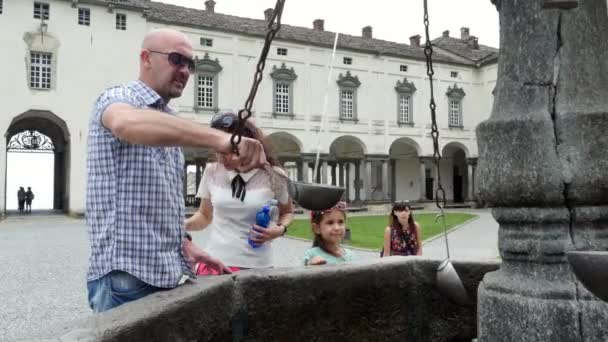 OROPA, BIELLA, ITALIE - 7 JUILLET 2018 : les gens boivent de l'eau alpine argentée dans des seaux d'argent, de la fontaine de masque gothique en pierre dans le sanctuaire d'Oropa, dans les montagnes près de la ville de Biella — Video