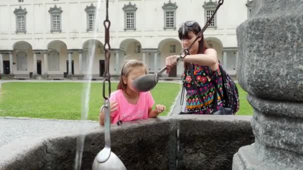 OROPA, BIELLA, ITALIA - 7 DE JULIO DE 2018: los turistas beben agua alpina de plata de cubos de plata, de la fuente máscara gótica de piedra en el Santuario de Oropa, Santuario, en las montañas cerca de la ciudad de Biella — Vídeos de Stock