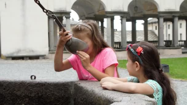 OROPA, BIELLA, ITALIA - 7 DE JULIO DE 2018: niñas niños beben agua alpina de plata de cubos de plata, de la fuente máscara gótica de piedra en el Santuario de Oropa, Santuario, en las montañas cerca de la ciudad de Biella — Vídeos de Stock