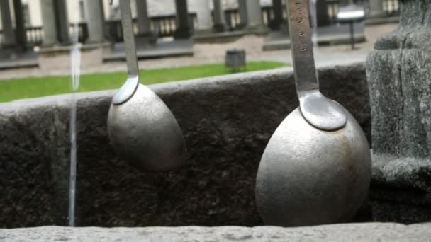 OROPA, BIELLA, ITALIA - 7 DE JULIO DE 2018: primeros planos, cucharones de plata antiguos, cuencos suspendidos de una antigua fuente de piedra con cadenas. Santuario de Oropa, santuario ubicado en las montañas — Vídeos de Stock