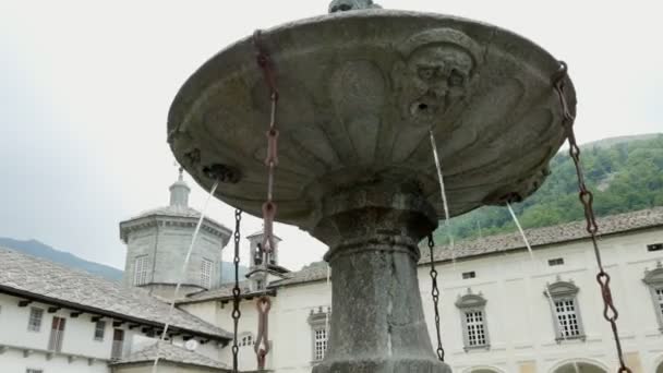 OROPA, BIELLA, ITALY - JULY 7, 2018: silver alpine water flowing from stone gothic mask fountain in Shrine of Oropa, Sanctuary, in the mountains near the city of Biella, Piedmont, Italy. — Stock Video