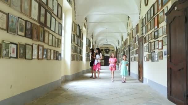 OROPA, BIELLA, ITALY - JULY 7, 2018: tourists, walk along long corridors, view pictures, photos on the walls. Shrine of Oropa, Sanctuary, in the mountains near the city of Biella, Piedmont, Italy. — Stock Video