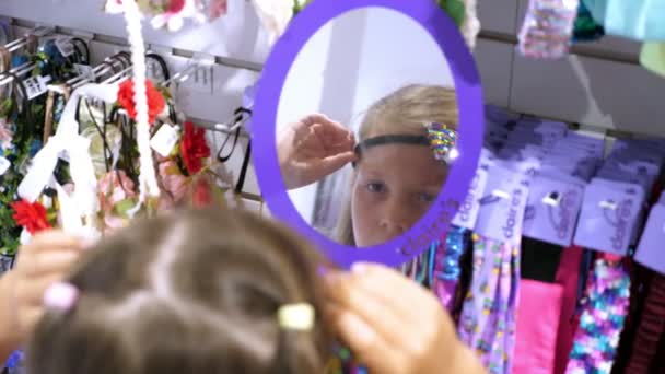 Einkaufen im Laden, Mädchen, Kind, wählt Haarnadeln, Gummibänder, Haarreifen, im Geschäft. Haarnadeln vor dem Spiegel anprobieren. Kleines Mode-Mädchen. Frauen Haar-Accessoires in Einkaufszentrum. — Stockvideo