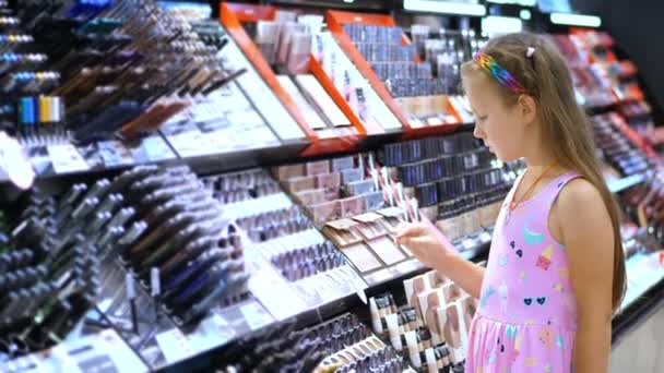 Κατάστημα καλλυντικών, όμορφο κορίτσι, kid, εξετάζει προσεκτικά τα καλλυντικά προϊόντα, σε κατάστημα ομορφιάς. Μόδα-κοριτσάκι — Αρχείο Βίντεο
