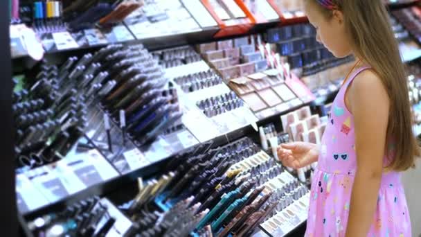 Kozmetikai bolt, csinos lány, kölyök, gondosan úgy véli, kozmetikai termékek, kozmetikai boltban. Kislány divat — Stock videók