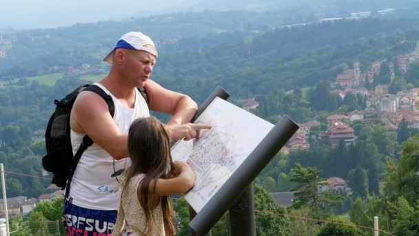 Beautiful park in alpine mountains. man and a girl, kid, tourists, study map of park, against backdrop of picturesque landscape of the Alpine mountains and a small town. summer hot day — Stock Video