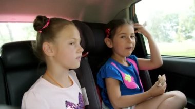 iki çocuk kız bir arabanın arka koltuğunda biniyor. Onlardan biri araba koltuğuna oturuyor, diğer, büyük kız yakın oturuyor. çocuklarla araba ile seyahat. yaz hafta sonu aile tatil gezisi