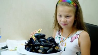 Yakın çekim, restoranda çocuk kız masada büyük bir kase pişmiş açık mavi midye bir tabak servis. Çocuk çok mutlu. nefis, büyük bölümü incelik