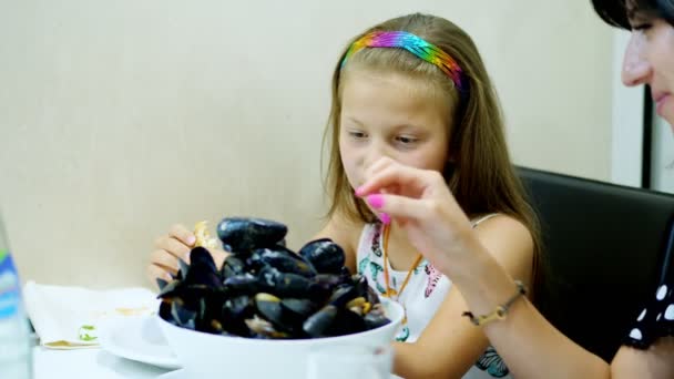 Close-up, no restaurante, a menina serviu na mesa uma tigela grande, um prato de mexilhões azuis abertos cozidos. criança muito feliz. grande porção de gostoso, delicadeza — Vídeo de Stock