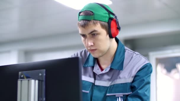 Portrait of an employee of an enterprise, factory. a worker in red headphones from noise, looks at a computer monitor, adjusts, controls work of machines, automated production. — Stock Video