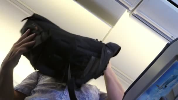 Hombre pone equipaje de mano en el estante superior en un avión de pasajeros. Vista inferior. Concepto de viaje . — Vídeo de stock