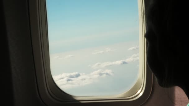 Primer plano. silueta oscura de niña mirando a través de la ventana de aviones ver cielo y nubes y paisaje por debajo — Vídeos de Stock