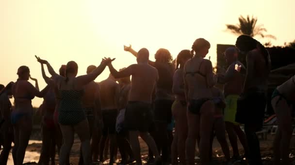 Siluetas oscuras de personas bailando, divirtiéndose en la playa, en verano, al atardecer. Fiesta de playa — Vídeos de Stock