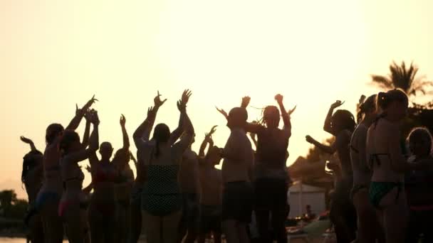 Siluetas oscuras de personas bailando, divirtiéndose en la playa, en verano, al atardecer. Fiesta de playa — Vídeos de Stock