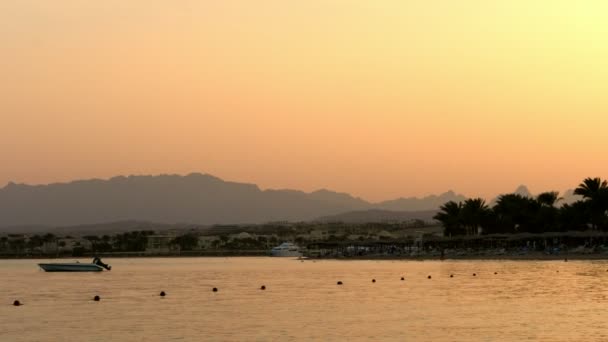 HURGHADA, EGITO - OUTUBRO 24, 2018: Uma das muitas enseadas tranquilas do Mar Vermelho, ao pôr-do-sol, ao entardecer. contra o pano de fundo dos contornos das montanhas, palmeiras . — Vídeo de Stock