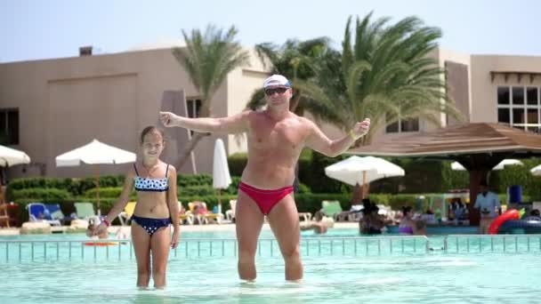 Uomo in occhiali da sole, padre e figlia, bambina, ballare nell'acqua della piscina, divertirsi insieme. Felice famiglia rilassante in piscina in una calda giornata estiva al parco acquatico . — Video Stock
