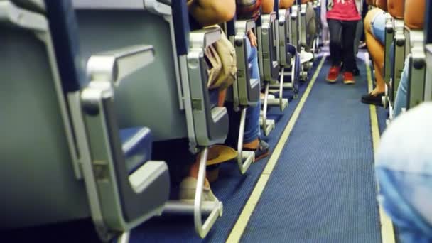 Ребенок идет через каюту самолета. видимы только ноги, интерьер самолета с пассажирами на сиденьях — стоковое видео