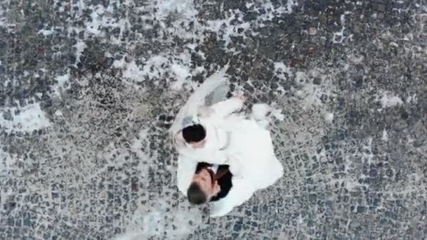 Winter wedding. Luchtfoto van jonggehuwde paar in trouwjurken zijn bruiloft dans dansen in een park met sneeuw bedekte, tegen de achtergrond van straatstenen — Stockvideo