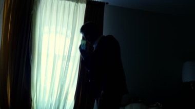 gece karanlığında, pencerenin karşısında karanlıkta. yakışıklı adam, bir smartphone cep telefonu üzerinde evde, onun yatak odasında konuşurken işadamı bir beyaz gömlek ve mavi ceket tutuyor