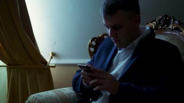 gece karanlığında, pencerenin karşısında karanlıkta. yakışıklı adam, bir smartphone, cep telefonu, sms, evde, onun yatak odasında gönderme işadamı bir beyaz gömlek ve mavi ceket tutuyor