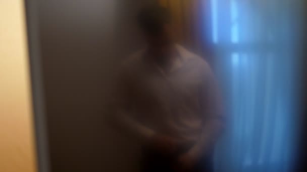 Размытый фокус, отражение в темном стекле. Красивый мужчина, молодой бизнесмен, в белой рубашке пристегивает ремень в брюках — стоковое видео