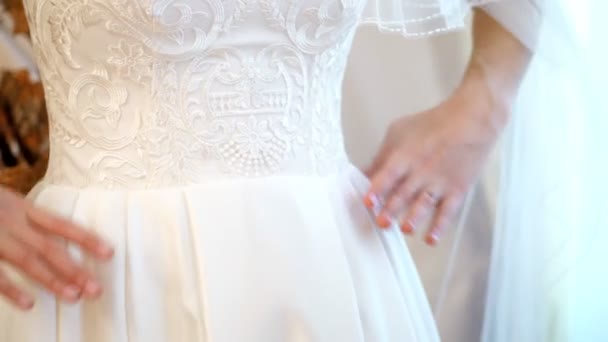 Vergoedingen van de bruid. de bruid is gekleed voor de bruiloft. Close-up van de handen van de bruiden met een zachte manicure, tegen de achtergrond van een jurk van wit kant. Bruiloft jurk details, close-up. — Stockvideo