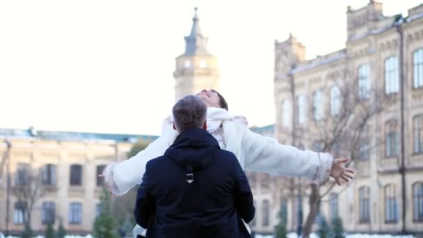 Winter wedding. newlywed couple in wedding dresses. groom holds bride in his arms, spinning. they are happy, smiling at each other. background of ancient architecture, snow-covered park, — Stock Video