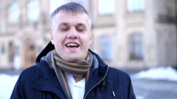 Retrato de um belo homem sorridente em um lenço e casaco bem abertos. inverno dia gelado . — Vídeo de Stock