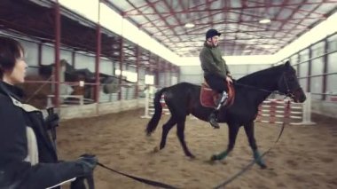 Özel hangarda bir Engelli genç hippoterapi yakın gözetim öğretmen ile bir ata binmek öğrenir. Sağ bacağı yerine yapay uzuv yaşamalı. hayvanlarla Engelli rehabilitasyonu