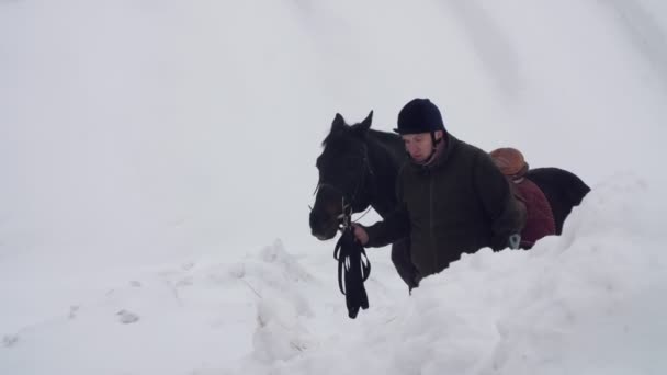 Mroźną zimę, niepełnosprawny mężczyzna jockey prowadzi, trzymając z stery czarny koń na drodze. człowiek ma protezy zamiast prawej nogi. pojęcie rehabilitacji osób niepełnosprawnych ze zwierzętami. Hipoterapia — Wideo stockowe