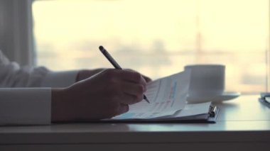 yakın çekim, kadın el, siyah kalem tutan ve bir şeyler yazıyor belgeleri, grafikleri ve diyagramları, beyaz bir masaüstü ofis ile çalışan iş kadın.