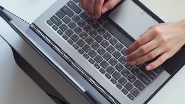 Primer plano, las manos de las mujeres están escribiendo algo en un teclado gris portátil, en un escritorio blanco . — Vídeos de Stock