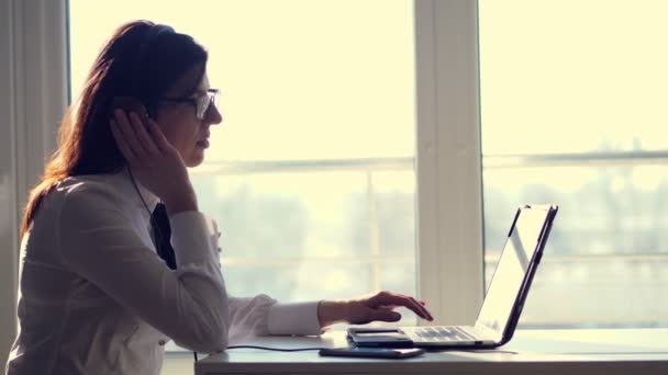 Zijaanzicht van focus attente vrouwelijke succesvolle dispatcher, het dragen van de koptelefoon, kijkt naar scherm, op een computer, laptop op kantoor werkt. Call center operator, of onderwijs op web, raadpleegt — Stockvideo