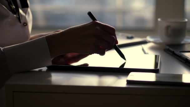 Temná silueta podnikatelka, closeup z rukou. píše něco v tabletu, dále je laptop na stole. Pozadí rozmazané okna, paprsek světla se odráží v obrazovky tabletu — Stock video