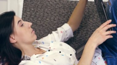 Genç kadın, kız, beyaz gömlek ve pantolon kanepeye, küçük yalan esmer, laptop ile kanepe. müzik, monitör, dizüstü bilgisayar ekran görünüyor. dekoratif duvar beyaz arka plan üzerinde