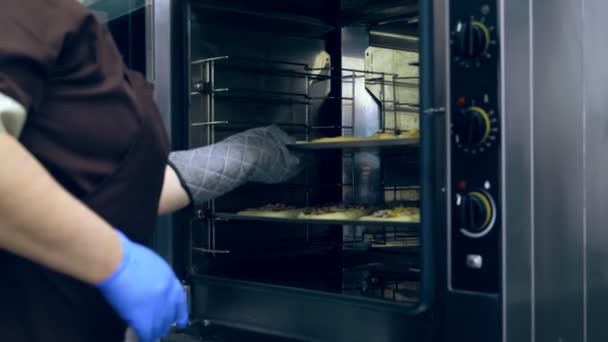 Close-up, the cook puts in a large industrial oven, a baking tray with buns, pizza made with yeast dough, for baking, cooking. Baking bread in industrial restaurant kitchen, bakery using commercial — Stock Video