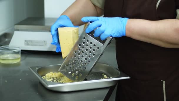 Nahaufnahme, ein Koch in Handschuhen reibt den Käse auf einer Reibe, bereitet das Gericht vor. — Stockvideo