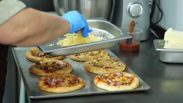 Nahaufnahme, das Kochen mehrerer Mini-Pizza aus Hefeteig mit Wurst und Käse. Koch bestreut Pizza mit Käse. Prozess des Kochens Bäckerei, in Messehalle, restauriert. — Stockvideo