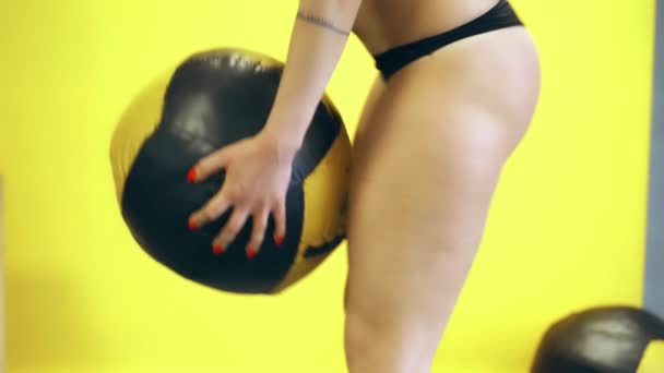 Close-up, uma mulher em tangas pretas e top de esportes, faz, executa exercícios com uma bola pesada. O conceito de um corpo bonito, desportivo, tonificado e atraente. mulher bonita com quadris atraentes, entra para — Vídeo de Stock